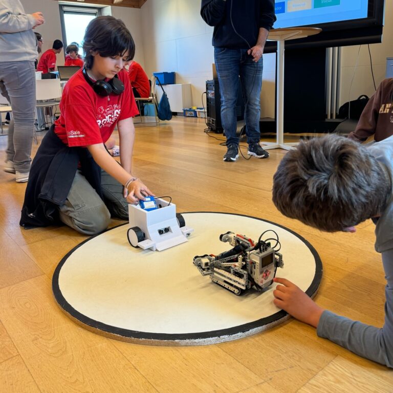 Participant posicionant un robot d'impressió 3D a la pista circular de sumo de robots davant d'un Lego Mindstorms, durant una competició de robòtica educativa